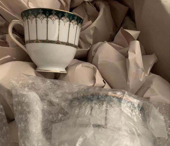 Close up of a coffee cup from the first picture in a container with all the clean and protectively wrapped dishes in the cont