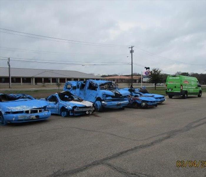 SERVPRO of Waco green van and a line of heavily damaged vehicles which have been repainted the same color blue.