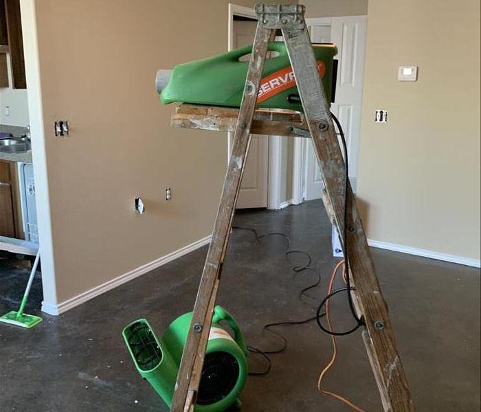 Picture shows an ozone machine on a ladder with an air mover (commercial fan) blowing near it